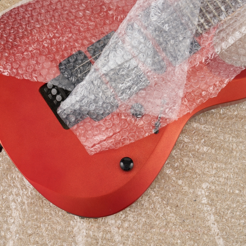 gitarre-in-luftpolsterfolie-verpackt Ein roter E-Gitarrenkorpus, teilweise in Luftpolsterfolie eingewickelt, liegt auf einer Schutzschicht während des Verpackens und Transports.