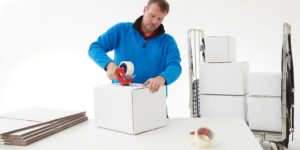 mezczyzna zaklejajacy bialy karton przezroczysta tasma nawinieta na dyspenser