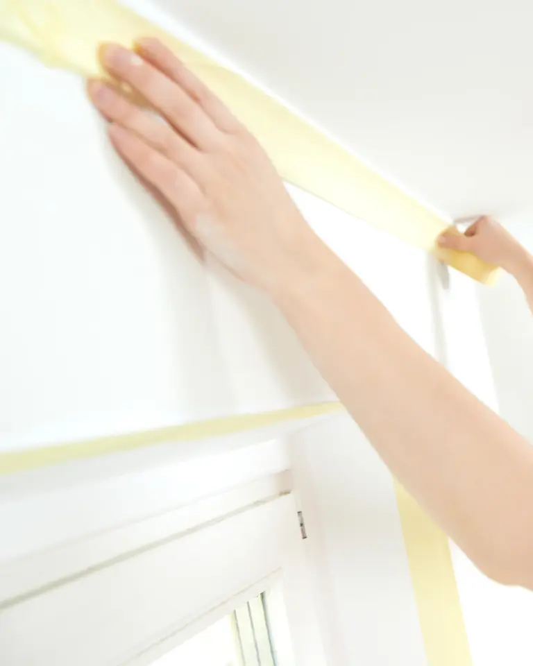 a woman applying masking tape to a wall