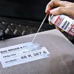 Mann sprueht Klebstoffentferner auf eine Oberflaeche