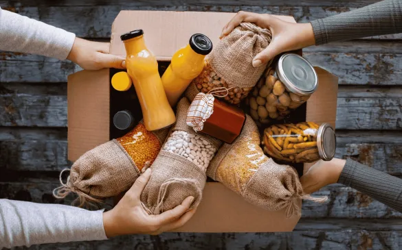 Zapakowane do kartonu produkty spożywcze – butelki z sokiem, słoiki z oliwkami i suche produkty