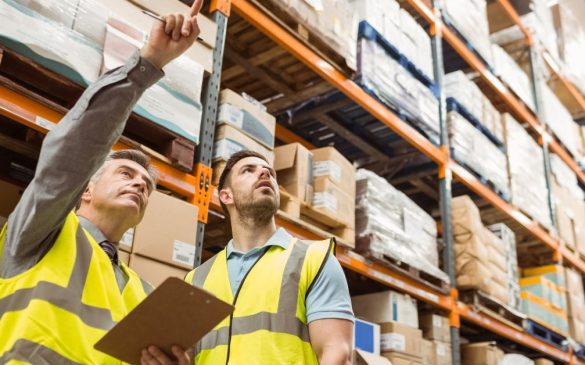 dwóch pracowników magazynowych wskazuje coś palcami w prawą stronę stojąc na środku magazynu