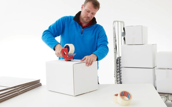 mezczyzna zaklejajacy bialy karton przezroczysta tasma nawinieta na dyspenser